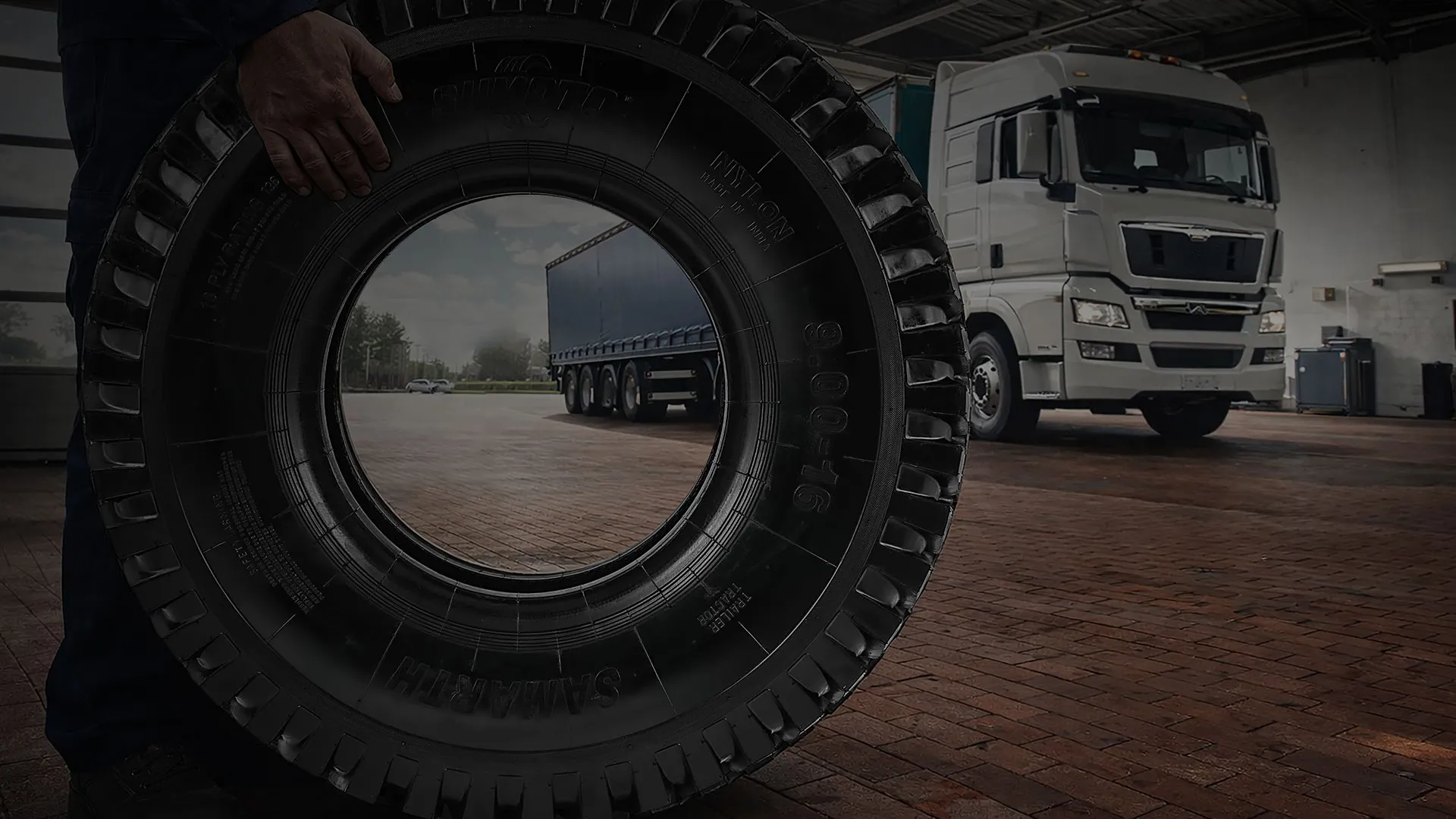 Technician rolling a Sumoto truck tyre in front of a haulage trailer